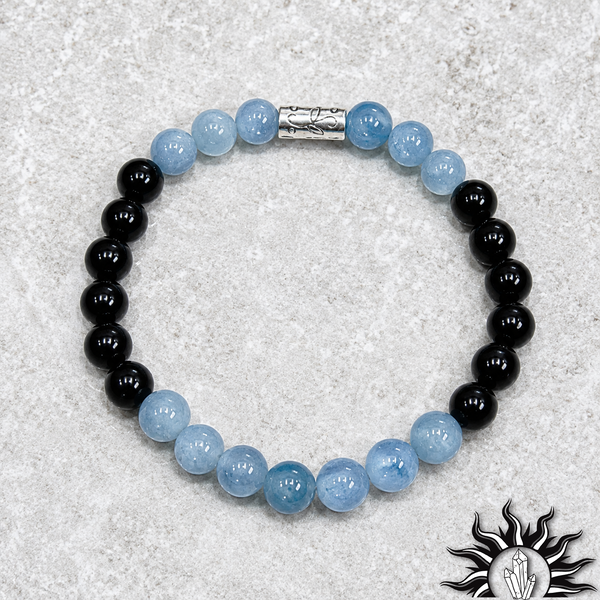 Close-up of a light blue aquamarine and black bead bracelet with a sterling silver engraved spacer, worn on a woman’s wrist. The bracelet features polished round beads with a soft glossy finish, styled against a neutral background for a clean, minimal jewelry presentation.