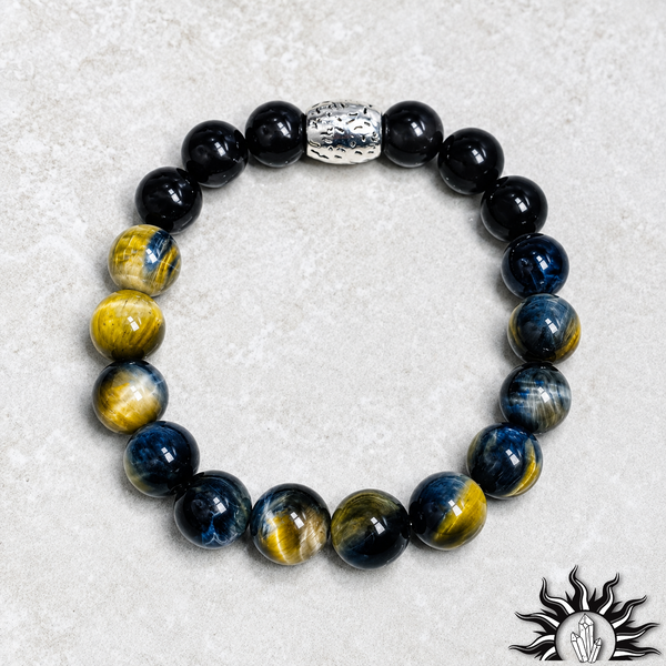 A beaded stretch bracelet featuring black round beads, blue and gold tiger's eye beads, and a textured silver accent bead, displayed on a light gray textured background.